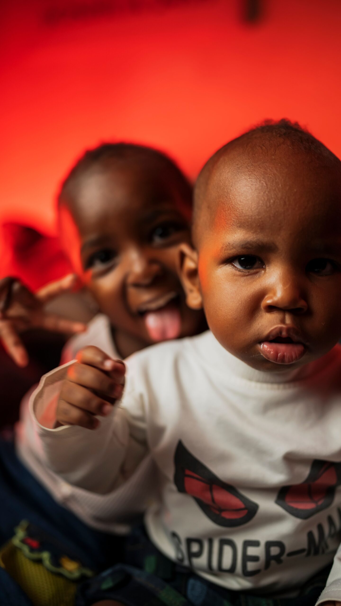 Two playful children having fun indoors with a vibrant red background in Nairobi, Kenya.