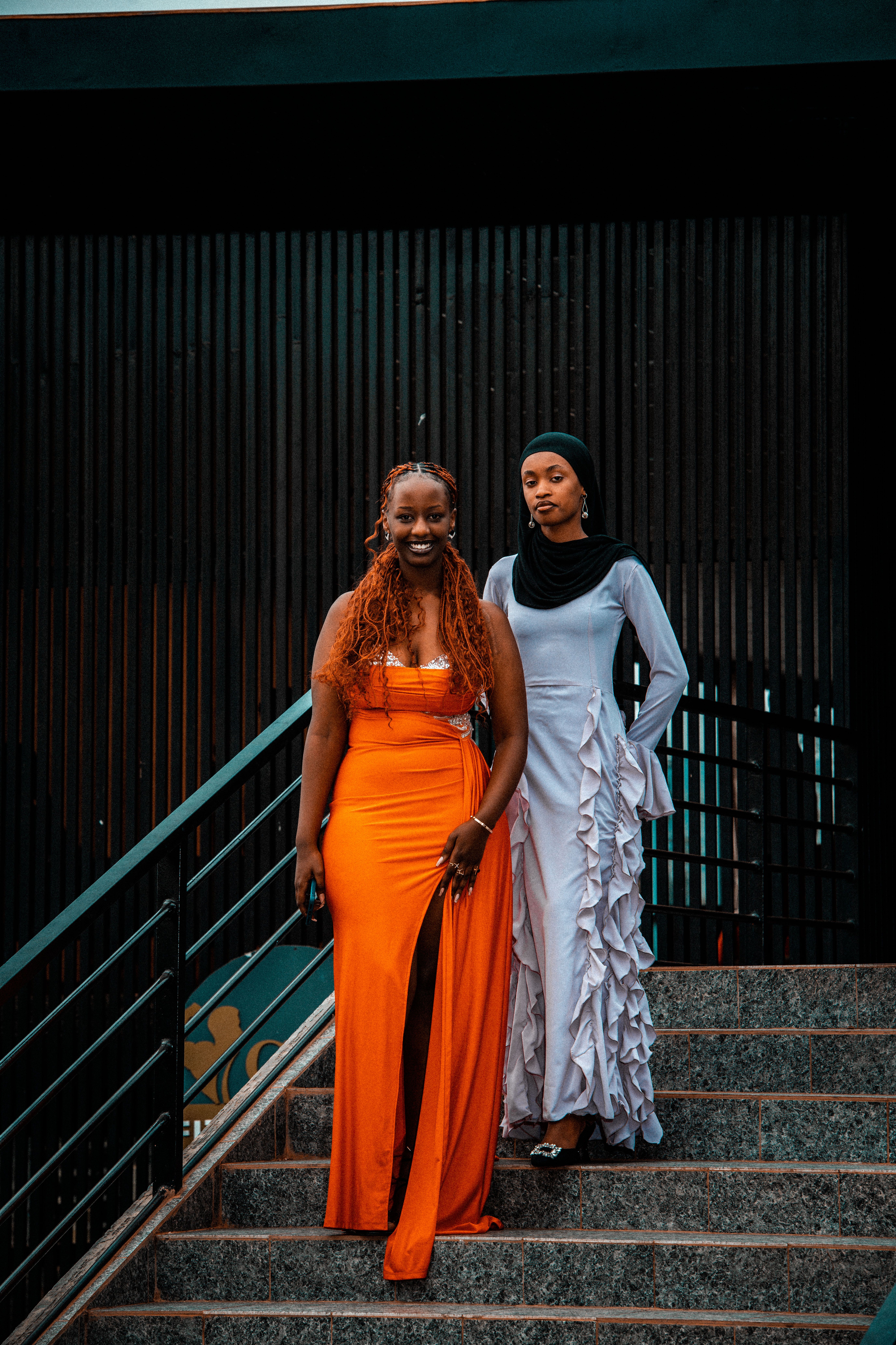 Two fashionable women in bright dresses descend a staircase, showcasing urban elegance in Rwanda.