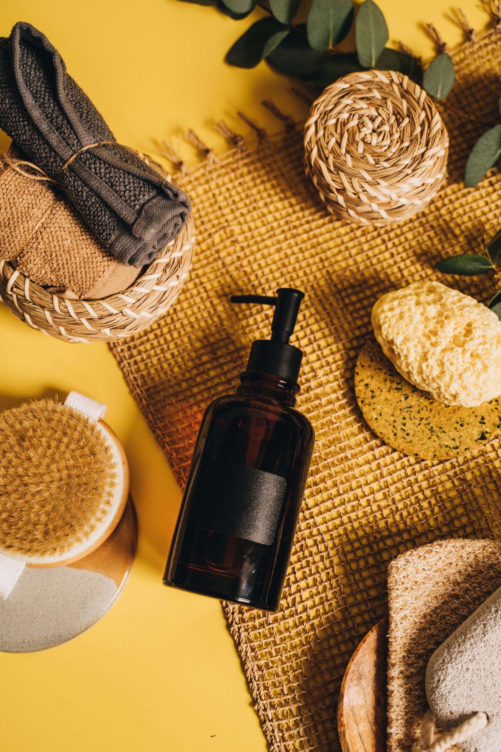 Flat lay of spa essentials including sponges and a dispenser on a yellow background.